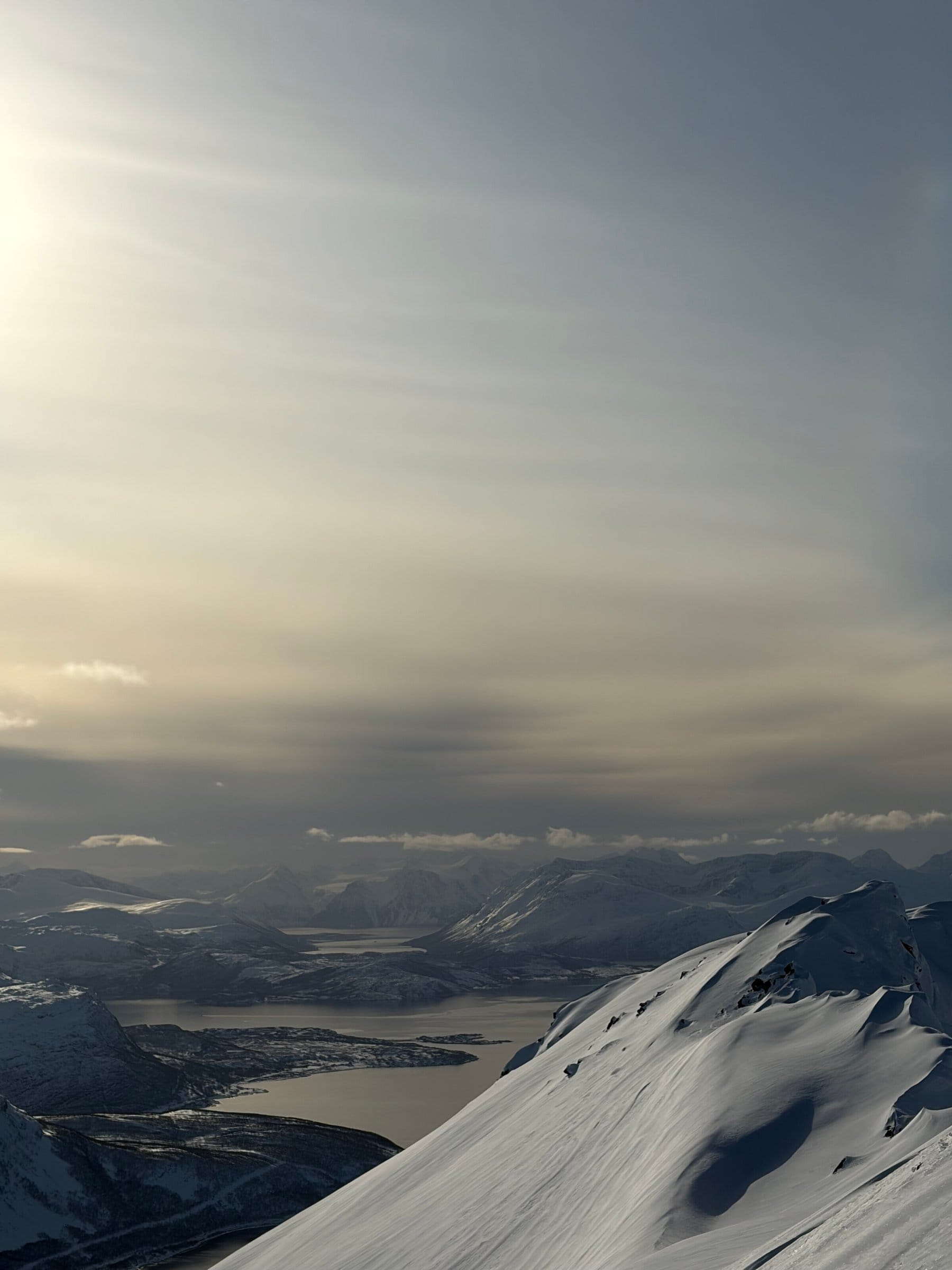 Snødekt fjelltopp med utsikt over fjorder og fjellrekker i Troms