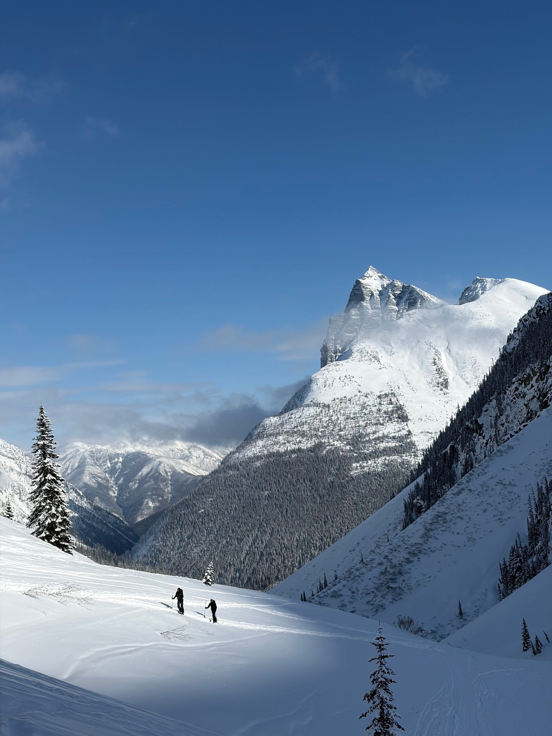To toppturløpere på vei gjennom uberørt snø med mektig fjelltopp i bakgrunnen