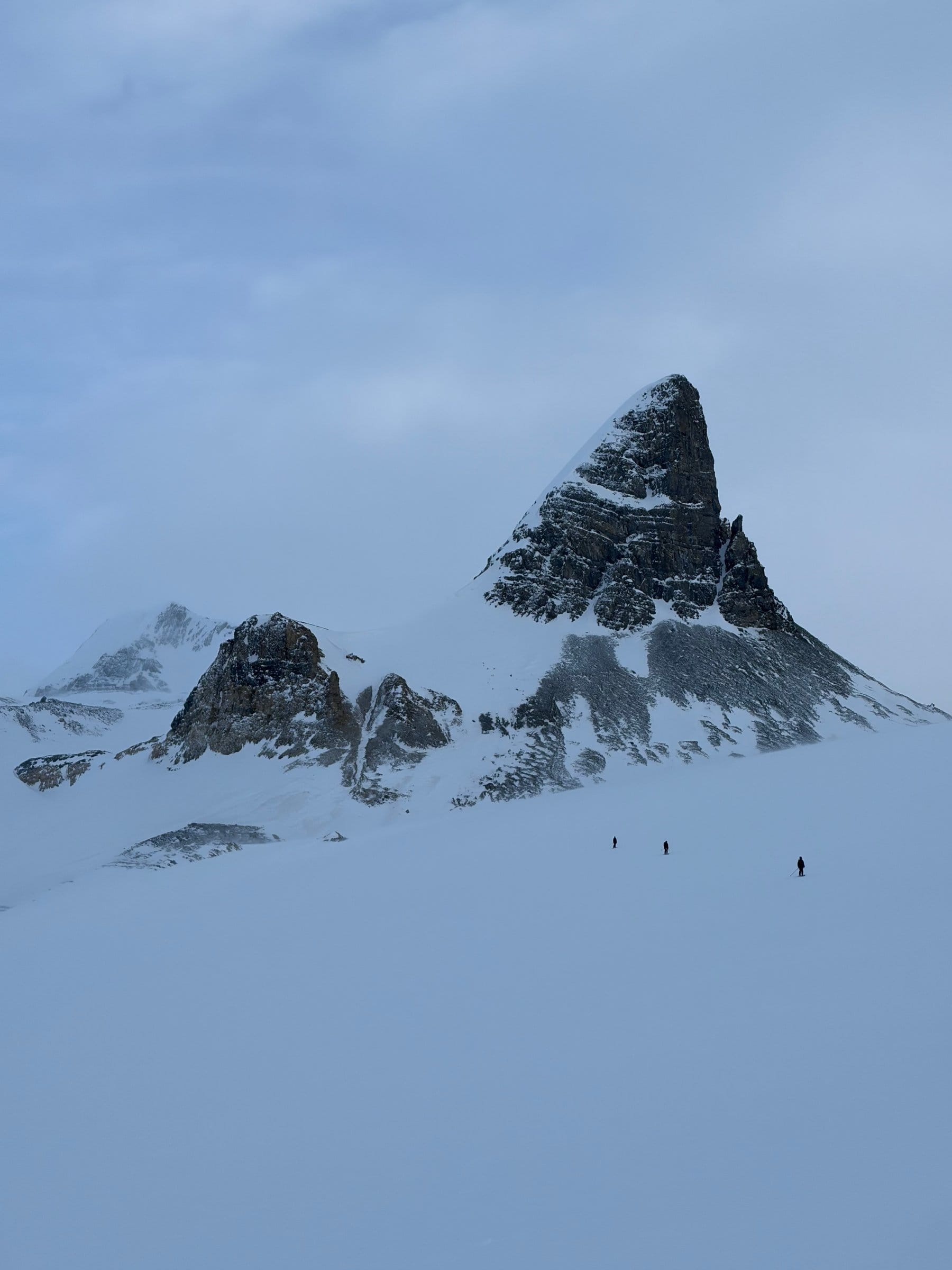 Dramatisk pyramidetopp med bittesmå skiløpere som krysser en isbre