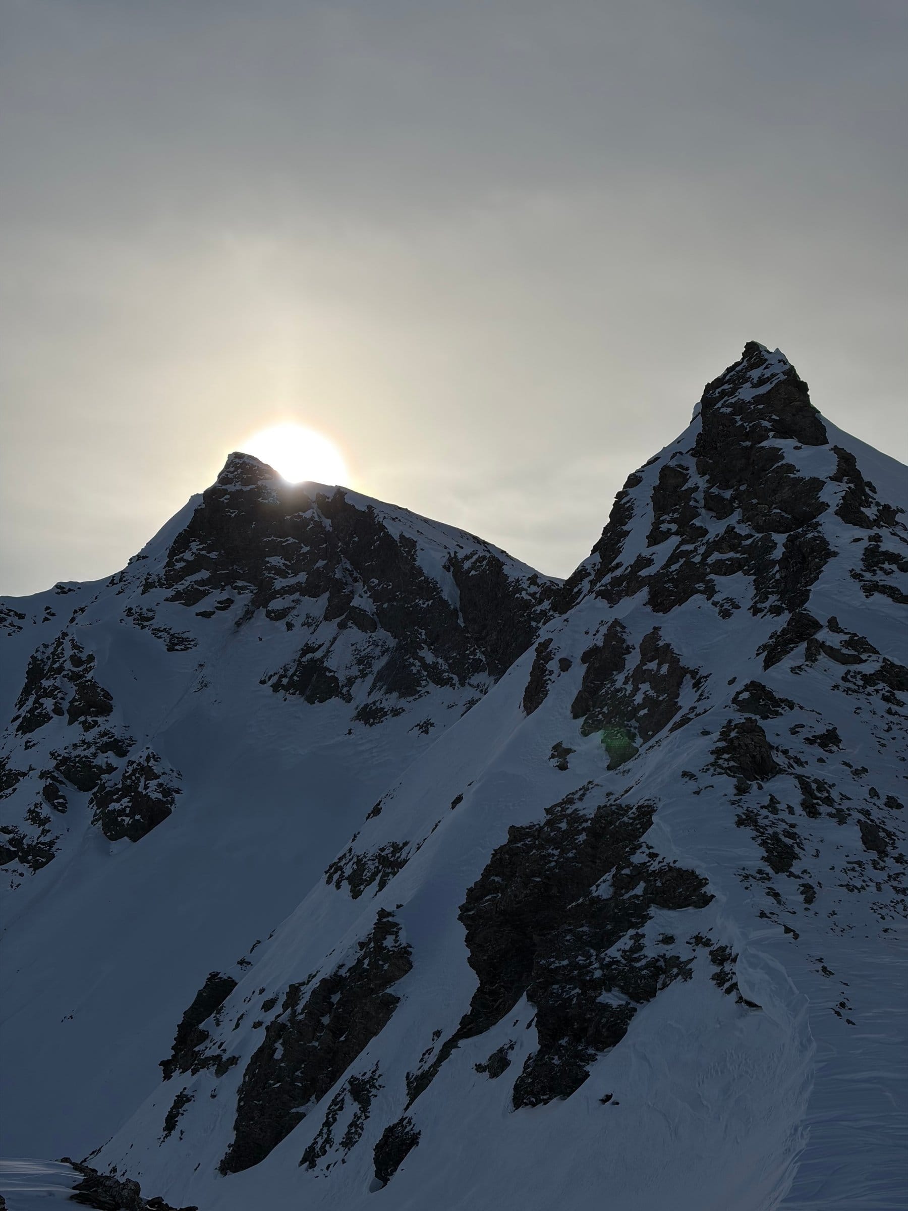 Solen går ned bak en snødekt fjellegg