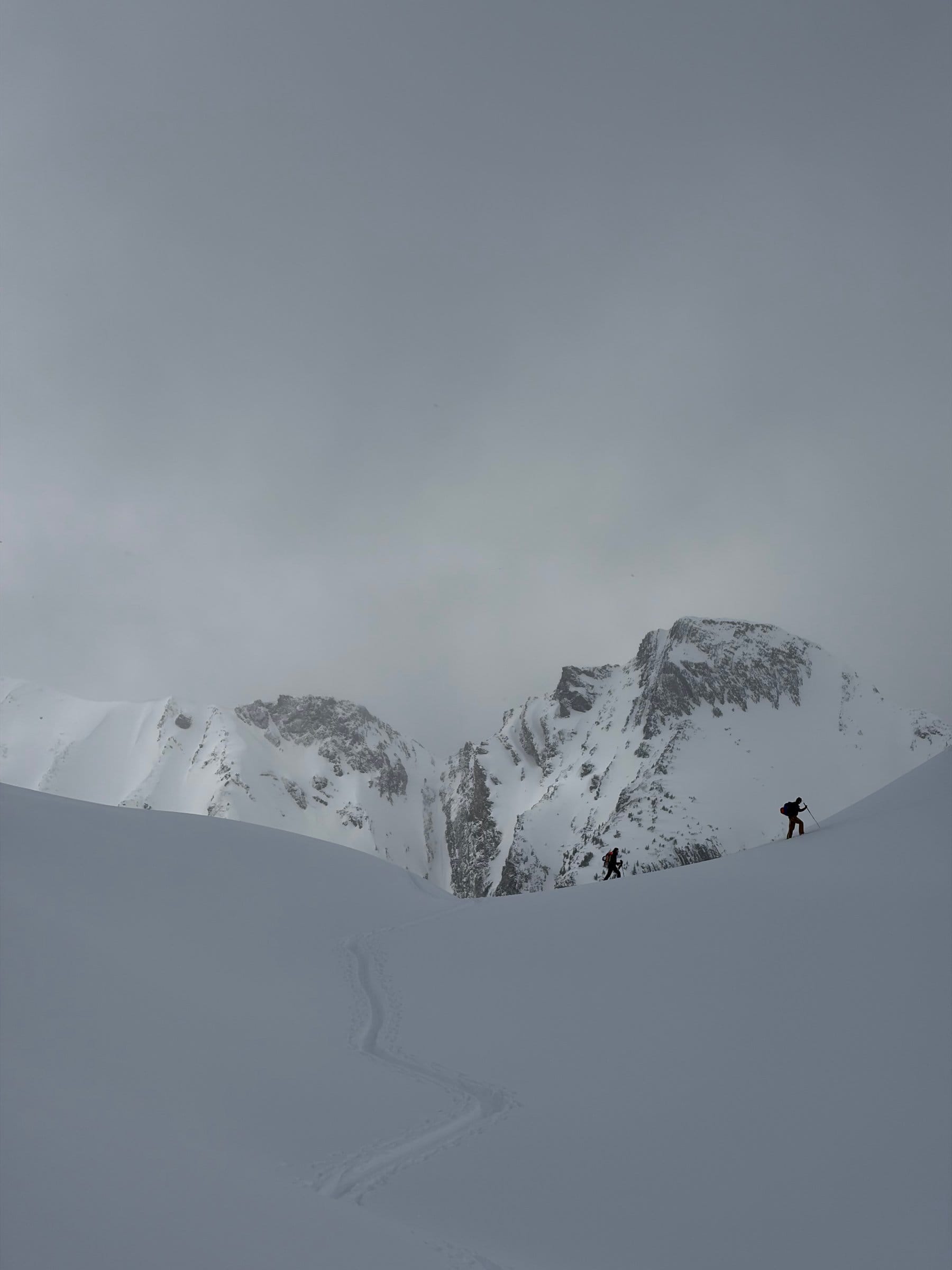 To toppturløpere på vei opp gjennom stemningsfullt alpint terreng med spor i nysnø