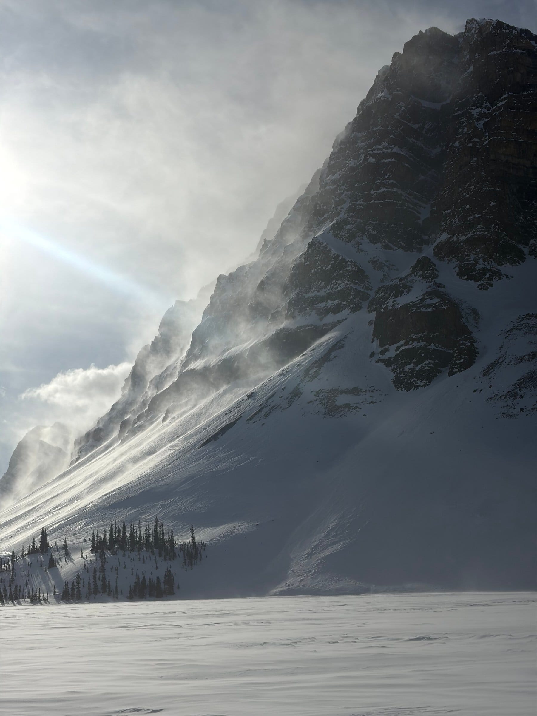 Dramatisk fjellvegg med snøfokk og sollys som bryter gjennom